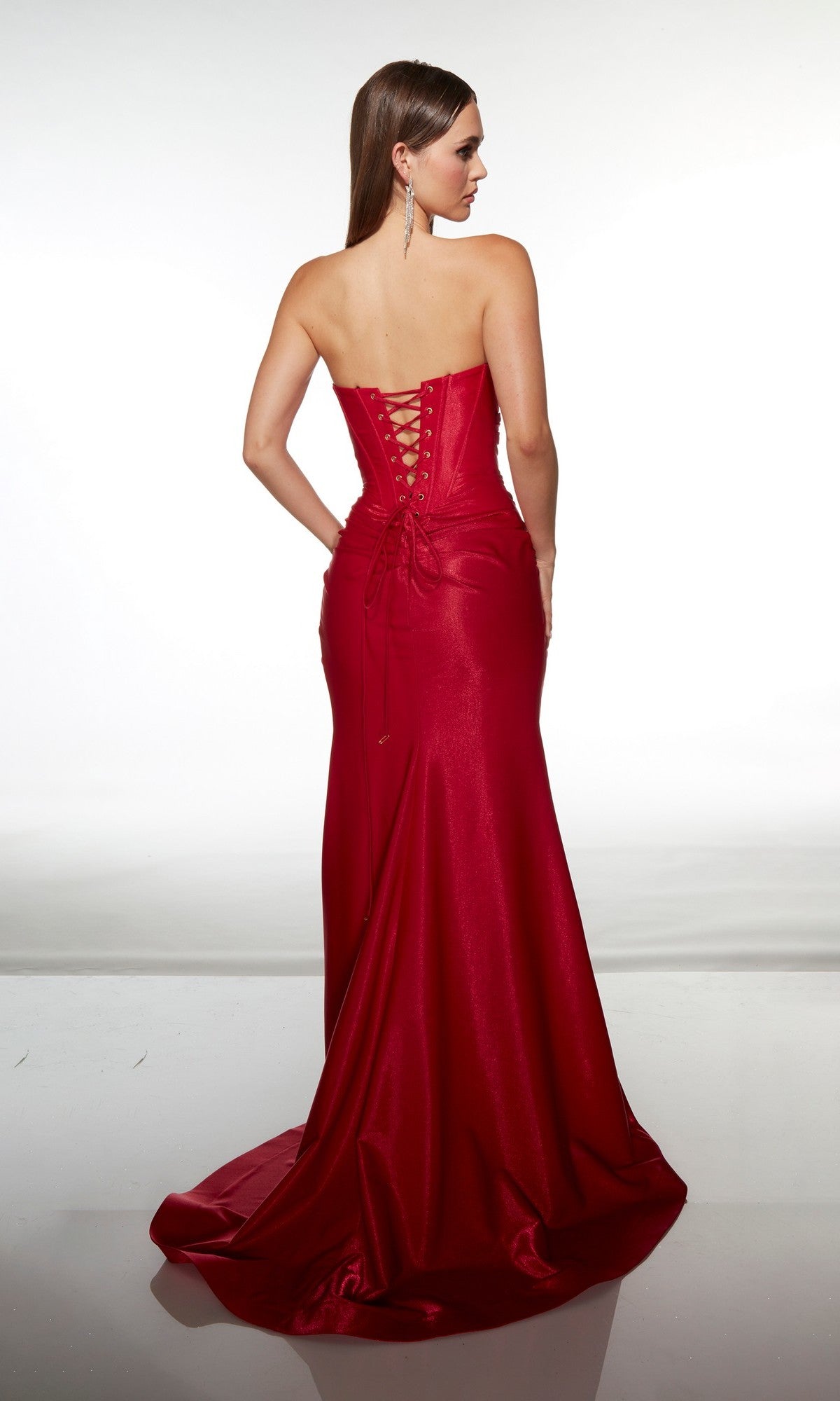 A woman stands on a reflective surface, facing away, wearing the Alyce 62128 long formal dress—a strapless, floor-length red satin gown with a sweetheart neckline and lace-up back.